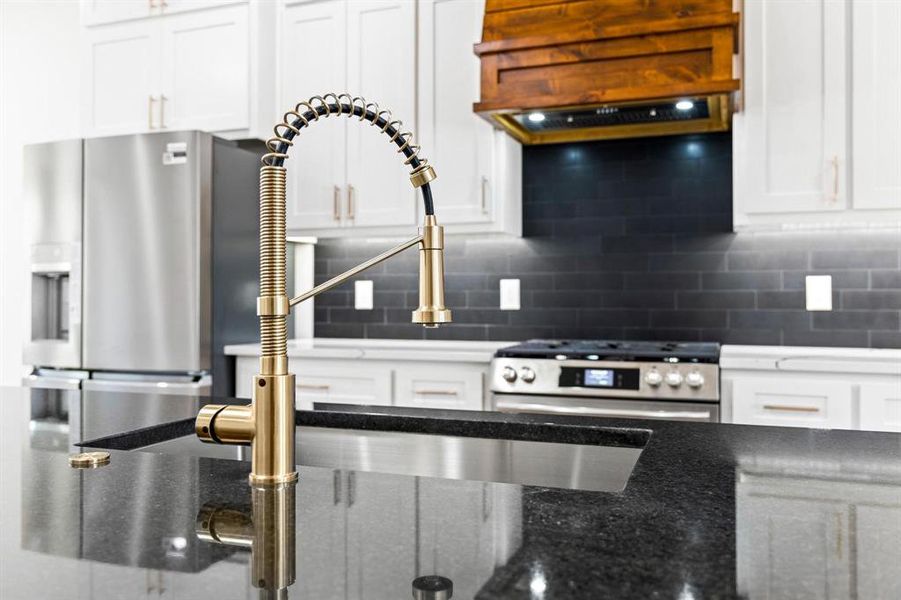 Kitchen featuring stainless steel stove, tasteful backsplash, custom range hood, and white cabinets