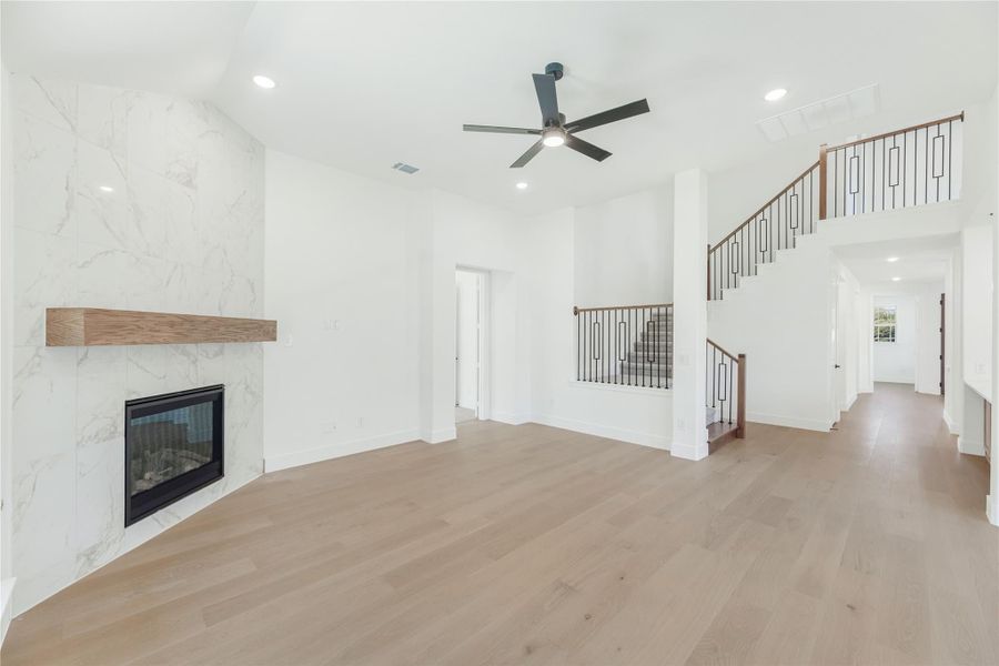 Open living room with marble fireplace, wood floors, ceiling fan, and staircase with iron railings Open living room with marble fireplace, wood floors, ceiling fan, and staircase with iron railings