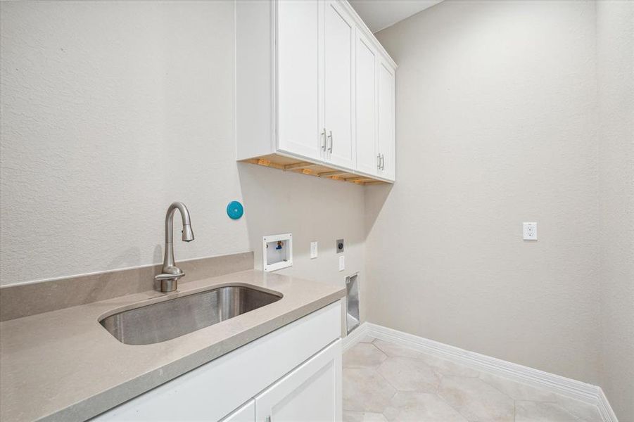 This is a modern laundry room featuring quartz countertop, white cabinetry, a stainless-steel sink with a sleek faucet. The room has tiled flooring and is well-lit.