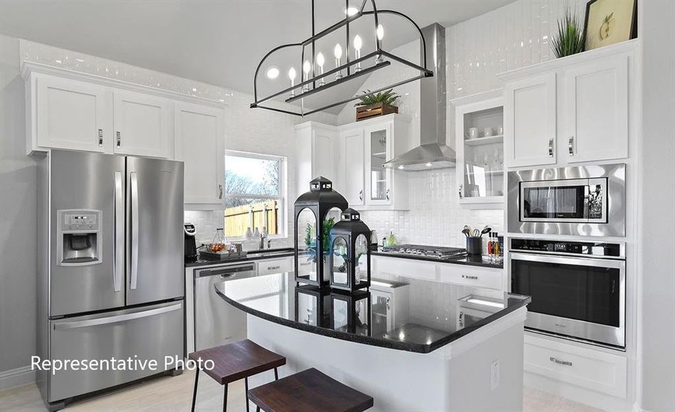 Modern kitchen featuring a central island with a dark countertop, stainless steel appliances, white cabinetry, a decorative pendant light fixture, and a white subway tile backsplash