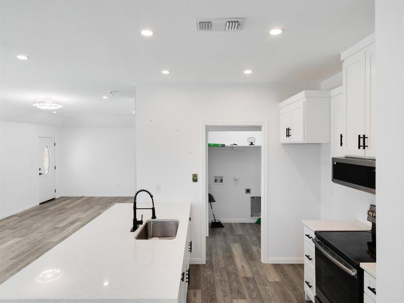 Contemporary kitchen featuring white cabinetry with black hardware, a stainless steel sink with a matte black faucet, and a white countertop island