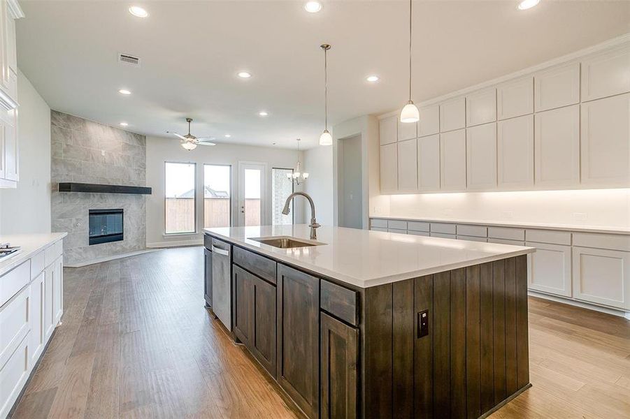 Kitchen featuring a fireplace, sink, dark brown cabinetry, light hardwood / wood-style floors, and a kitchen island with sink