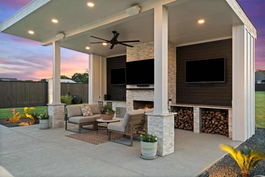 An inviting covered patio features a stone fireplace, multiple entertainment screens, and stacked firewood storage, perfect for outdoor gatherings. An inviting covered patio features a stone fireplace, multiple entertainment screens, and stacked firewood storage, perfect for outdoor gatherings.