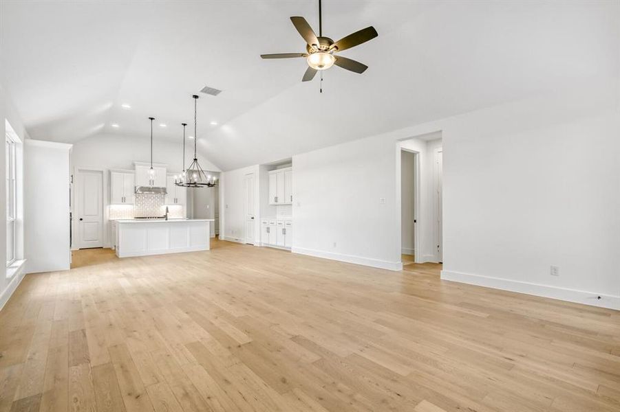 Unfurnished living room featuring suspended lighting, ceiling fan, light wood-type flooring, and lofted ceiling