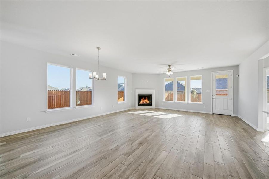 Unfurnished living room featuring a warm lit fireplace, light wood finished floors, a chandelier, and a ceiling fan Unfurnished living room featuring a warm lit fireplace, light wood finished floors, a chandelier, and a ceiling fan