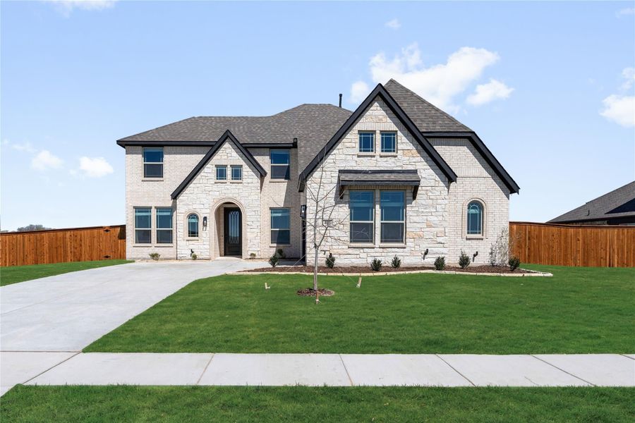 Two-story home with light stone exterior, arched entry, dark trim windows, and green front lawn Two-story home with light stone exterior, arched entry, dark trim windows, and green front lawn