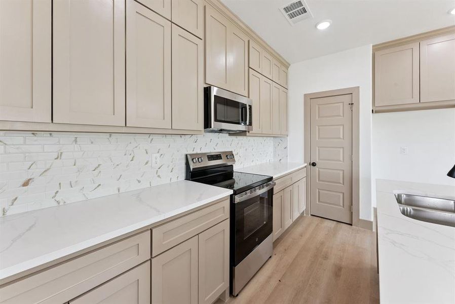 Kitchen featuring stainless steel appliances, tasteful backsplash, light wood-type flooring, light stone counters, and recessed lighting Kitchen featuring stainless steel appliances, tasteful backsplash, light wood-type flooring, light stone counters, and recessed lighting