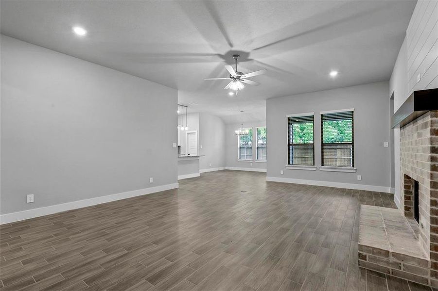 Unfurnished living room featuring a brick fireplace, ceiling fan with notable chandelier, and dark wood-type flooring