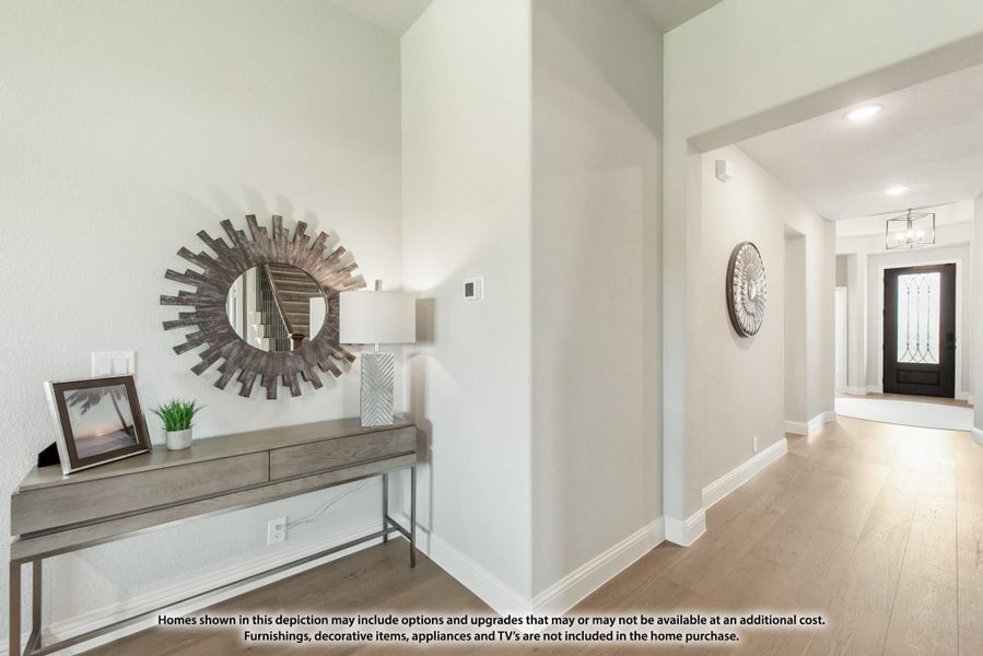 Entryway hallway with light wood floors, console table, sunburst mirror, and dark front door with glass panel
