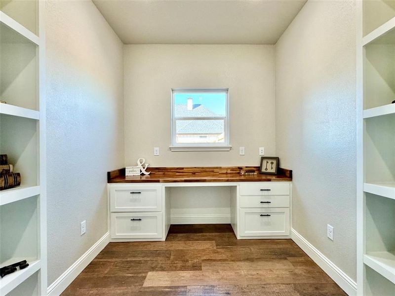 Unfurnished office featuring built in study area, built in shelves, dark wood-style flooring, and a textured wall