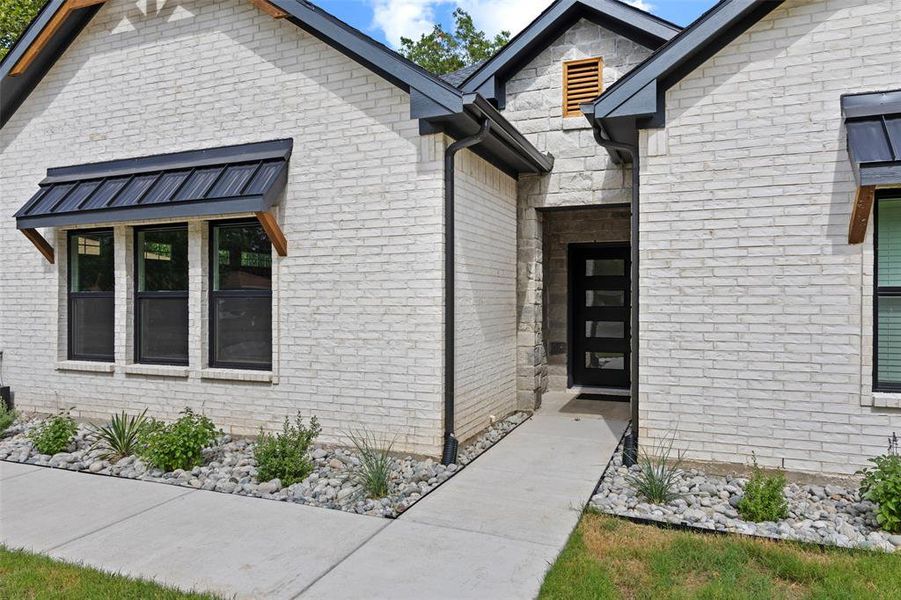 Contemporary facade featuring white brick, stone accents, black trim, and a prominent black entry door with horizontal lites
