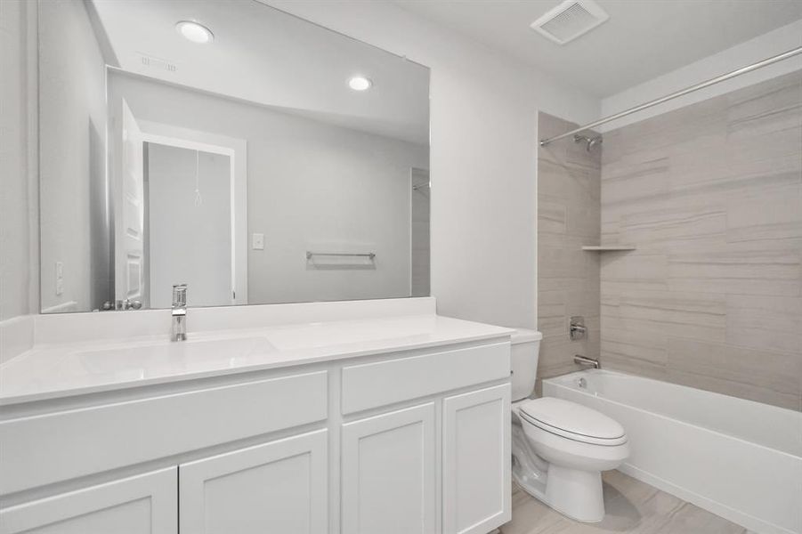 Secondary bathroom, where the tile flooring harmonizes with a bath/shower combo surrounded by tasteful tile. Light wood cabinets, coupled with a gorgeous countertop, elevate the space, cultivating a truly welcoming atmosphere. Sample photo of completed home with similar floor plan. As-built interior colors and selections may vary.