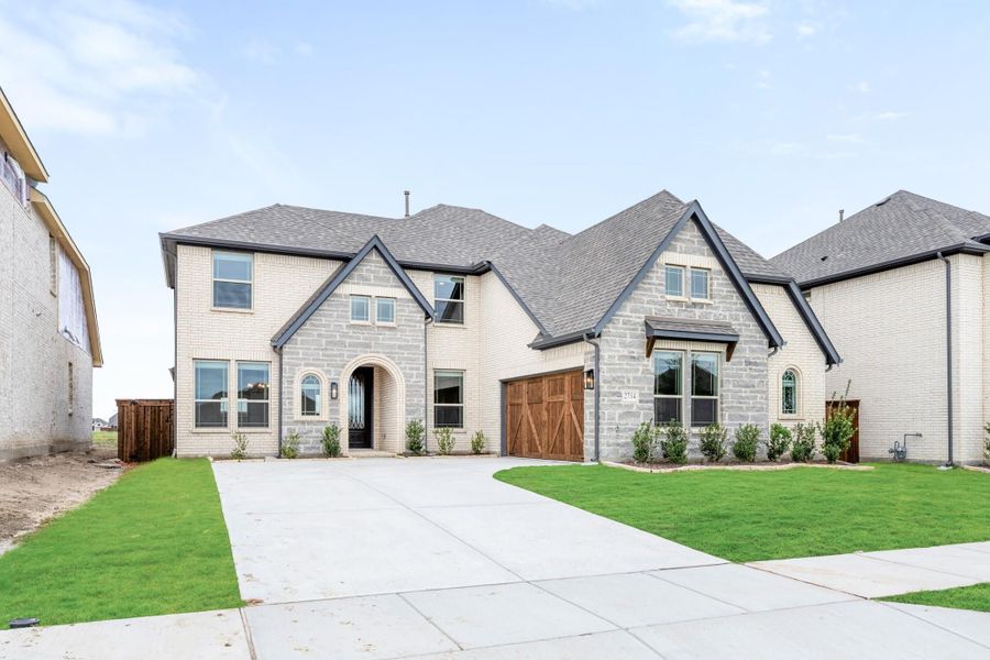 Two-story home with cream brick and stone exterior, wood garage door, arched entry, and manicured front lawn