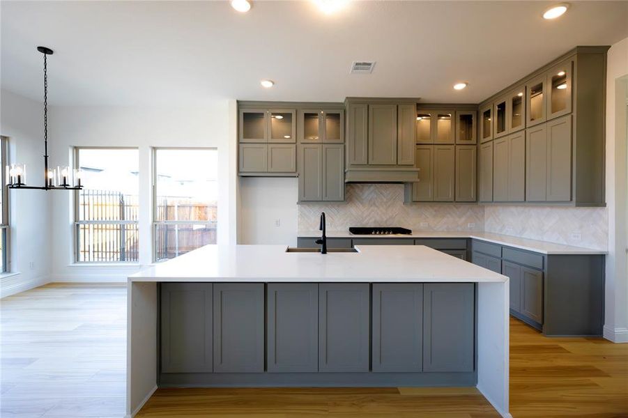 Kitchen with a kitchen island with sink, sink, light hardwood / wood-style floors, and hanging light fixtures