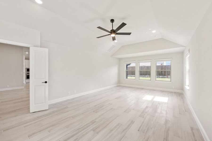 Empty bedroom with vaulted ceiling, ceiling fan, light wood floors, and backyard-facing windows Empty bedroom with vaulted ceiling, ceiling fan, light wood floors, and backyard-facing windows