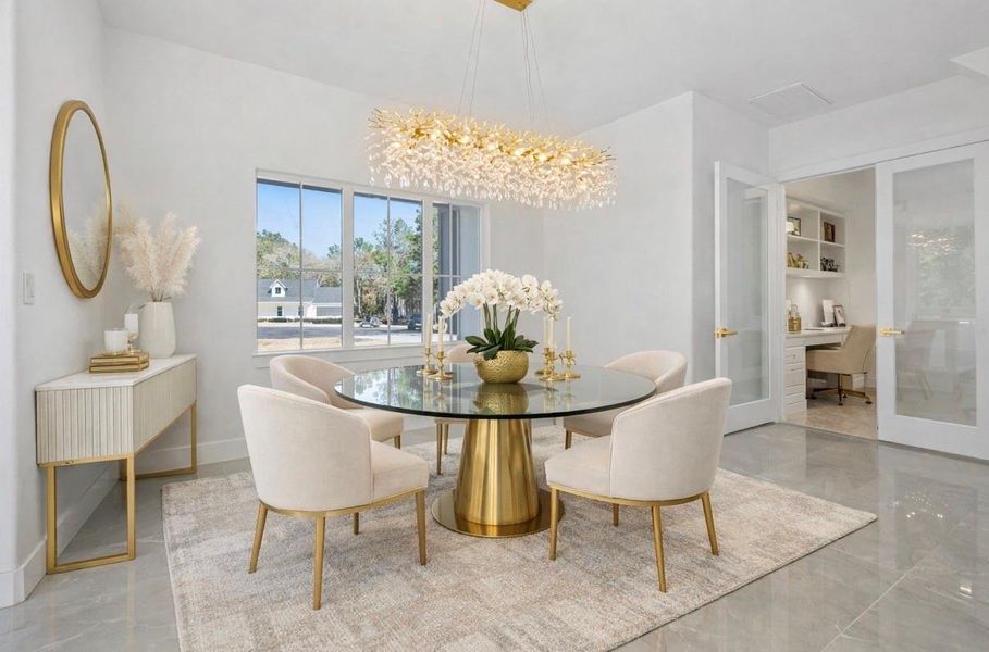 Bright, elegant dining area with a round glass table, gold base, and cream chairs under a modern chandelier. Natural light flows through the window, highlighting the neutral tones and sleek finishes. VIRTUALLY STAGED