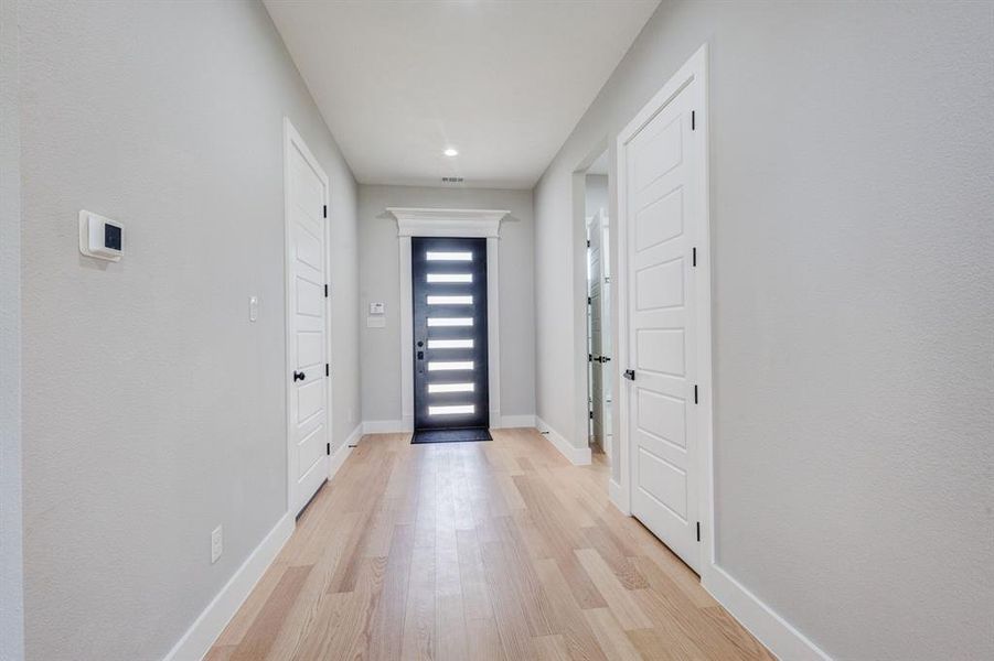 Entrance hallway featuring wood-finish flooring, a contemporary black entry door with frosted glass panels, white interior doors with black hardware, recessed ceiling lighting, and crisp white baseboards