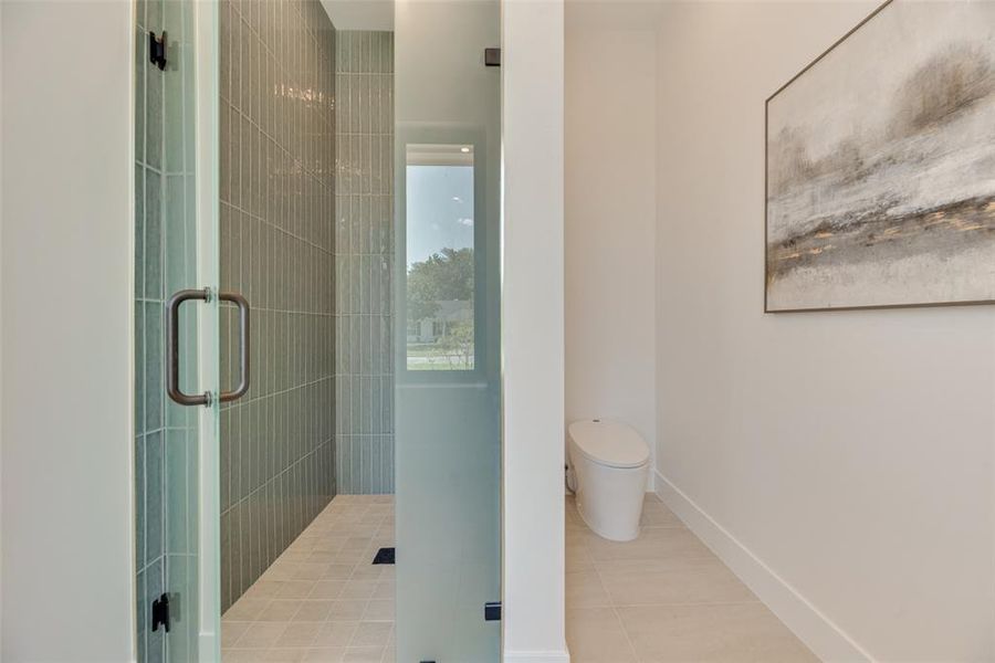 Bathroom with tile patterned floors, a shower with door, and toilet