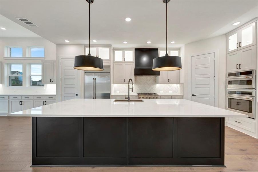 Kitchen with dual tone cabinets, a large island, light wood finished floors, glass fronted cabinets, and pendant lighting