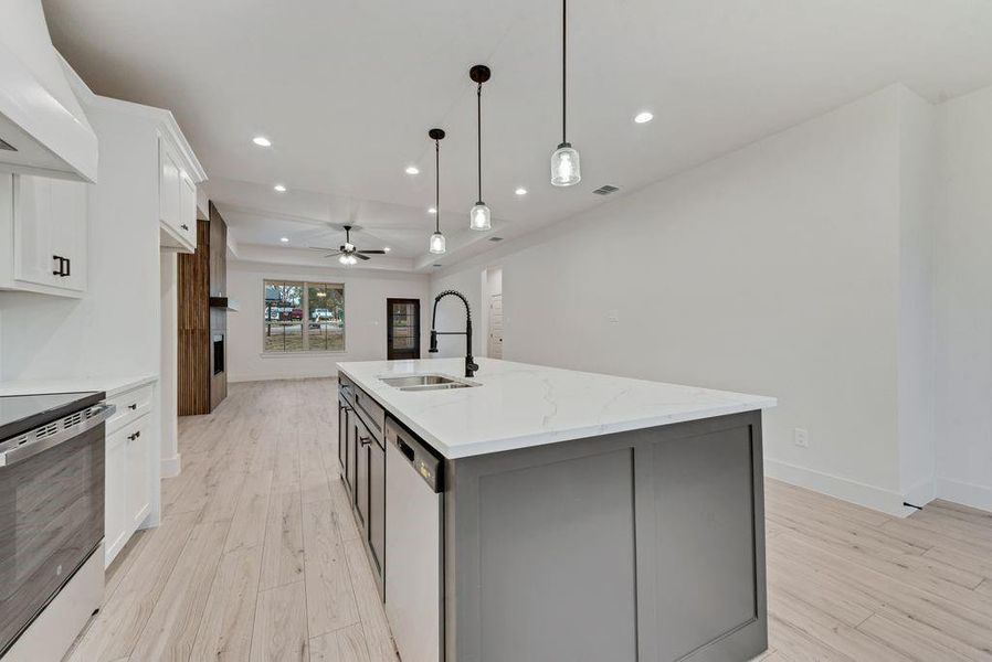 Kitchen featuring white cabinetry, appliances with stainless steel finishes, custom exhaust hood, hanging light fixtures, and light stone countertops