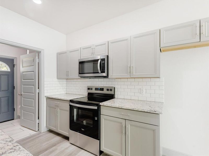 Kitchen featuring stainless steel appliances, light stone counters, decorative backsplash, light wood-type flooring, and gray cabinets