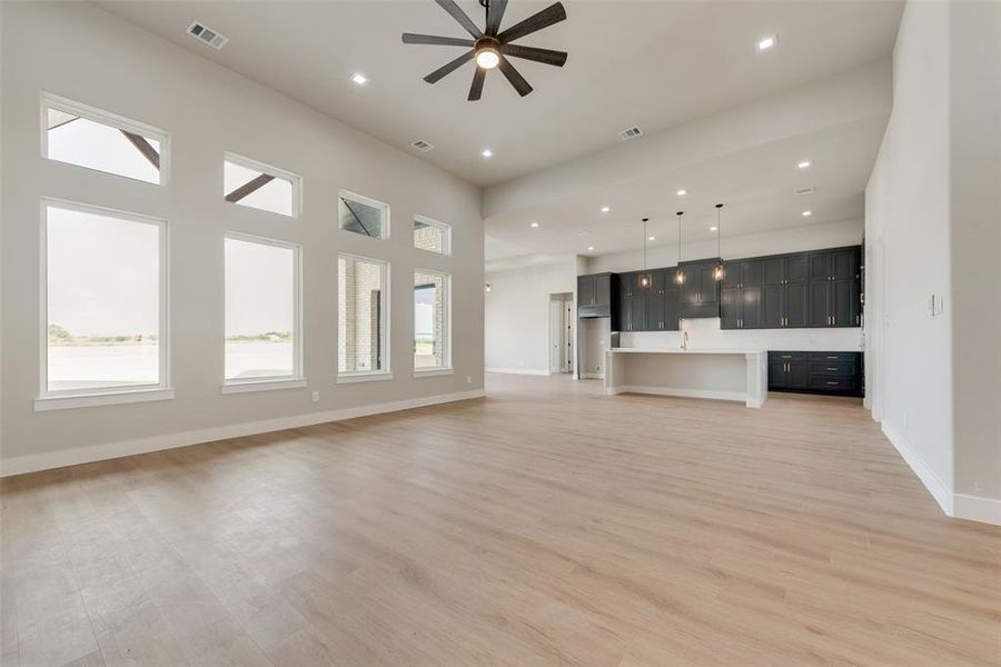 Unfurnished living room featuring ceiling fan, light hardwood / wood-style floors, and a towering ceiling