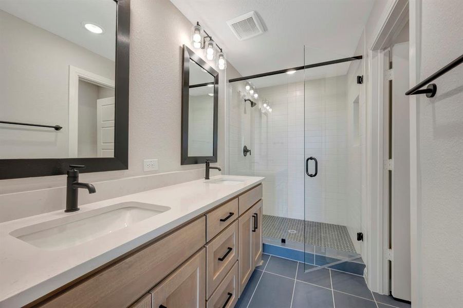 Full bath featuring double vanity, a stall shower, dark tile patterned floors, and a textured wall