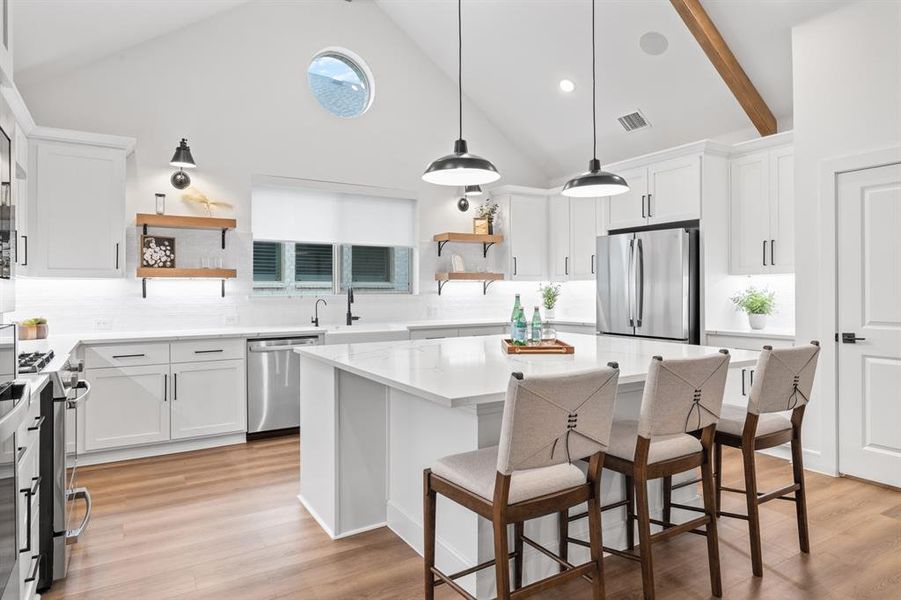 Kitchen featuring open shelves, white cabinetry, a kitchen bar, high vaulted ceiling, and a center island