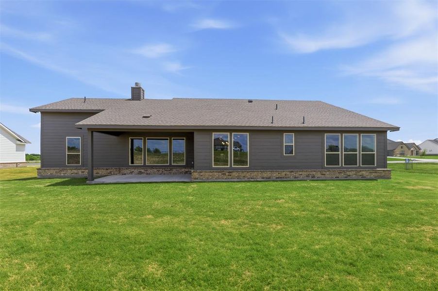Back of house featuring a patio, brick siding, a yard, a chimney, and roof with shingles