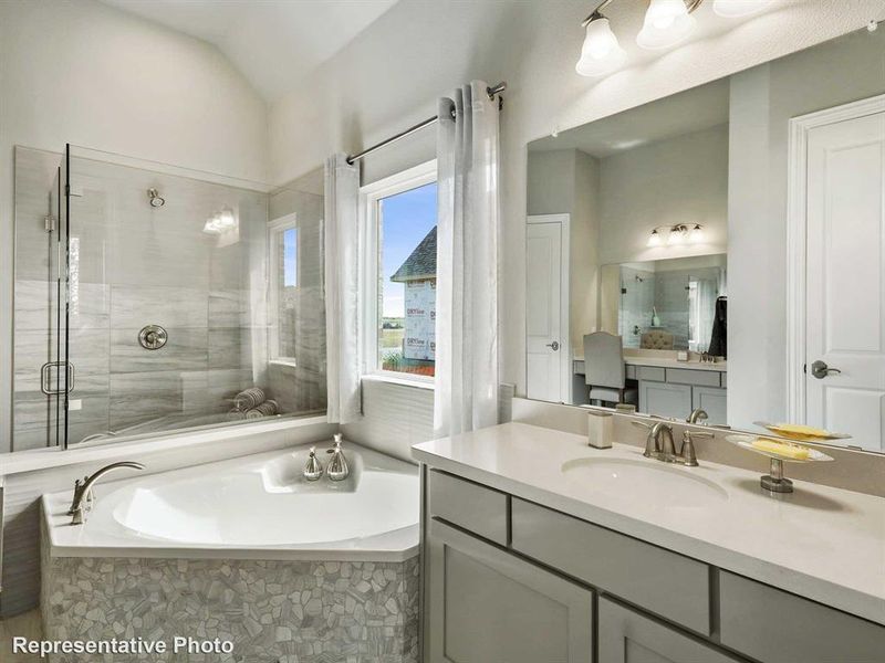 Bathroom featuring a corner soaking tub with pebble tile surround, a glass-enclosed shower with subway tile, a vanity with an undermount sink and ample counter space, and a large wall-mounted mirror