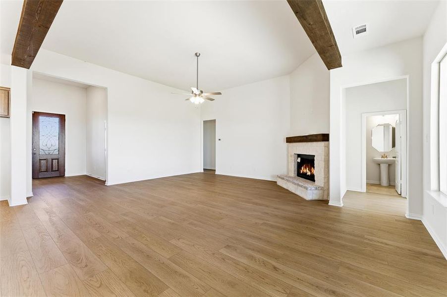 Unfurnished living room with beam ceiling, a lit fireplace, light wood-style flooring, and a ceiling fan