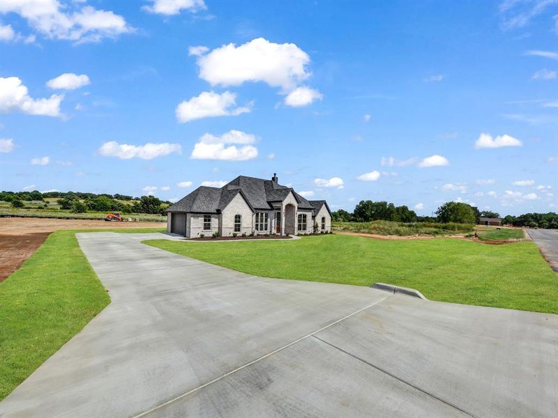 French country home with stone siding, concrete driveway, a chimney, a garage, and a front yard French country home with stone siding, concrete driveway, a chimney, a garage, and a front yard