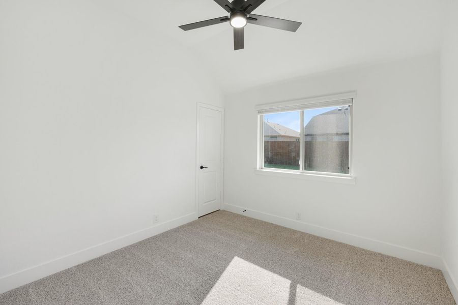 Empty bedroom with white walls, carpet flooring, ceiling fan, and a window with backyard view Empty bedroom with white walls, carpet flooring, ceiling fan, and a window with backyard view