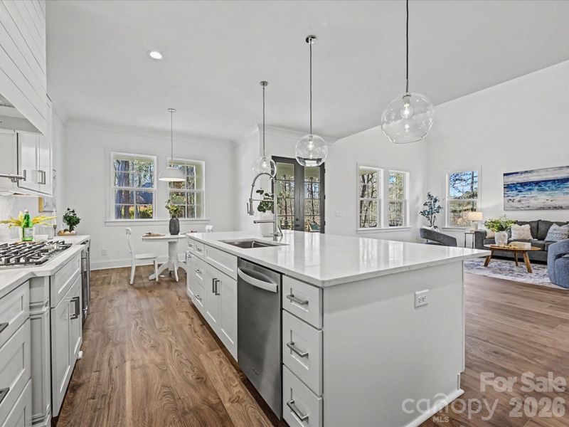 Bright open-concept kitchen with a large quartz island, stainless steel appliances, modern pendant lighting, and seamless flow into the main living area—ideal for entertaining.