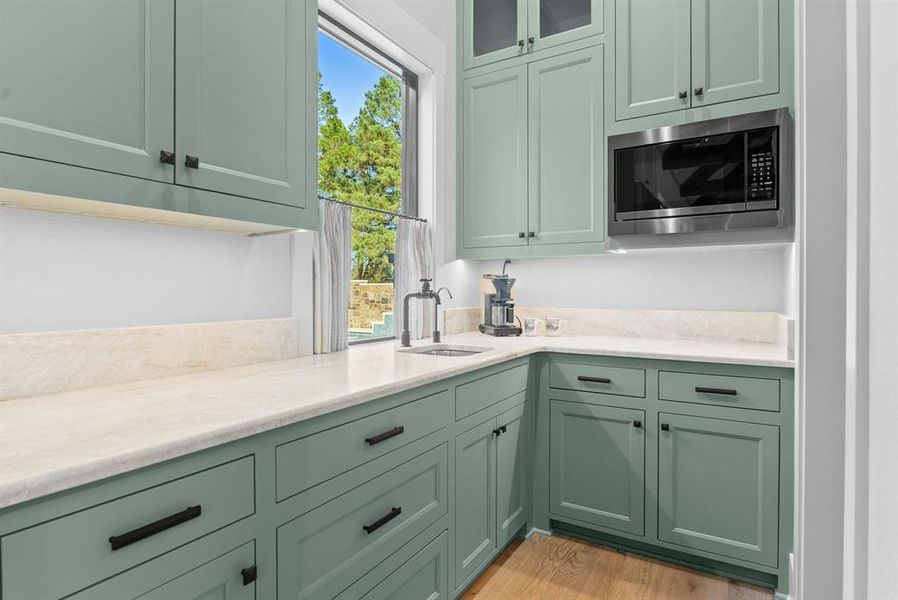 Kitchen featuring green cabinets, stainless steel microwave, glass insert cabinets, light stone counters, and light wood-style floors