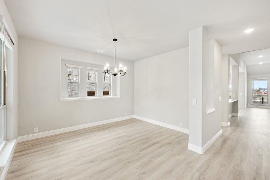 Empty dining room with light wood floors, chandelier, and white walls open to hallway Empty dining room with light wood floors, chandelier, and white walls open to hallway