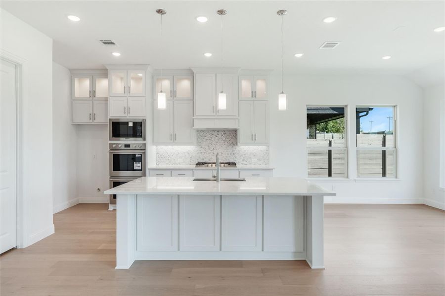 White kitchen with large center island, pendant lights, stainless steel appliances, and light hardwood floors