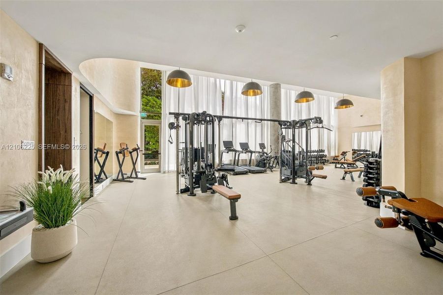Fitness center featuring floor-to-ceiling windows, large-format tile flooring, curved architectural detailing, and recessed dome pendant lighting Fitness center featuring floor-to-ceiling windows, large-format tile flooring, curved architectural detailing, and recessed dome pendant lighting