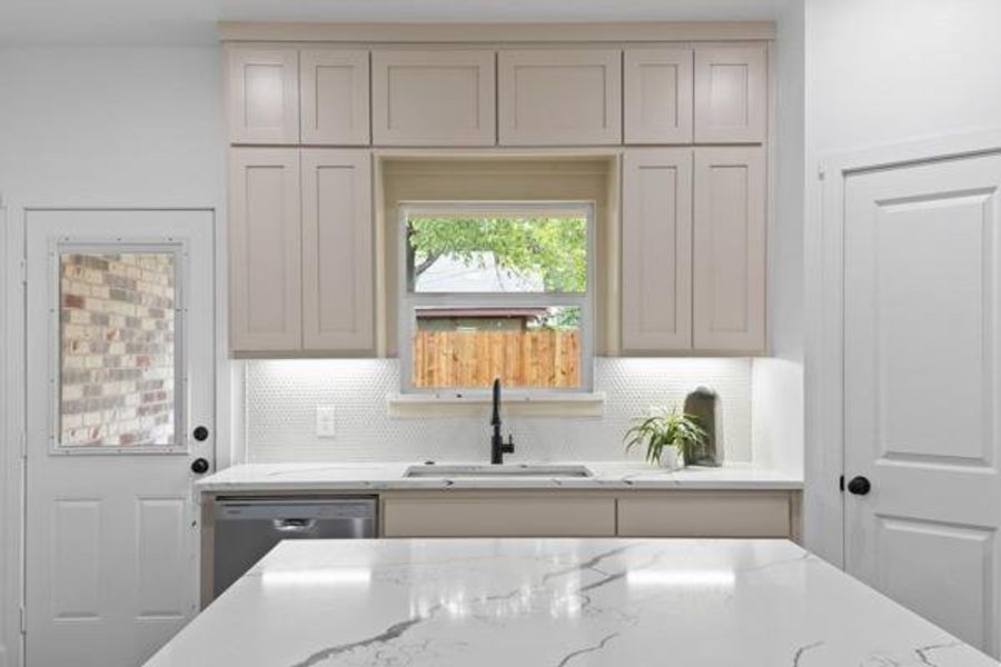 Kitchen featuring light-toned cabinetry, a white honeycomb tile backsplash, and a window above the sink Kitchen featuring light-toned cabinetry, a white honeycomb tile backsplash, and a window above the sink