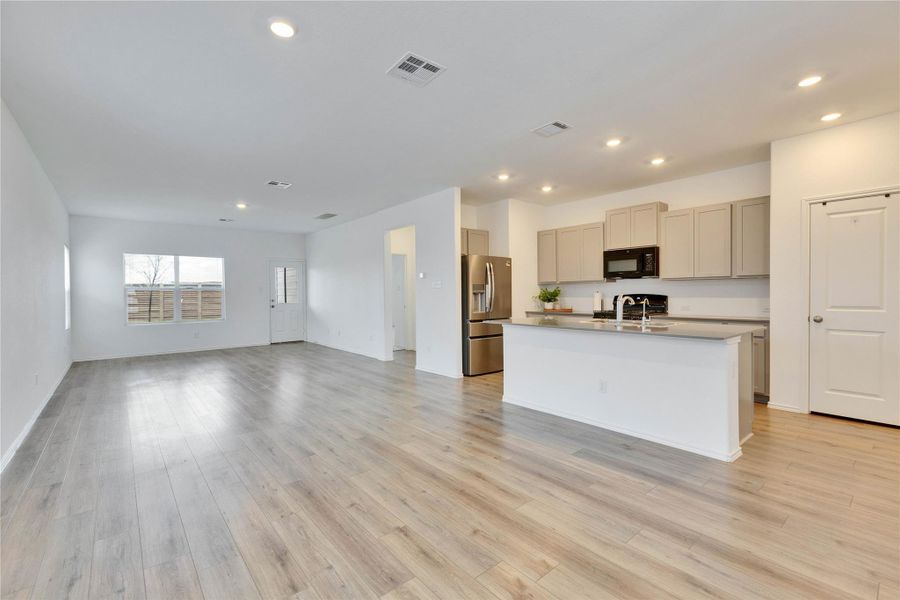 Kitchen with open floor plan, recessed lighting, stainless steel fridge with ice dispenser, black microwave, and an island with sink. Kitchen with open floor plan, recessed lighting, stainless steel fridge with ice dispenser, black microwave, and an island with sink.