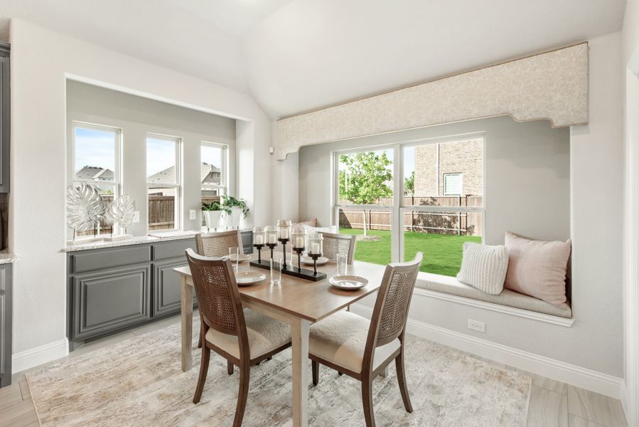 Dining area with wood table, cane chairs, built-in window seat, and large windows overlooking backyard