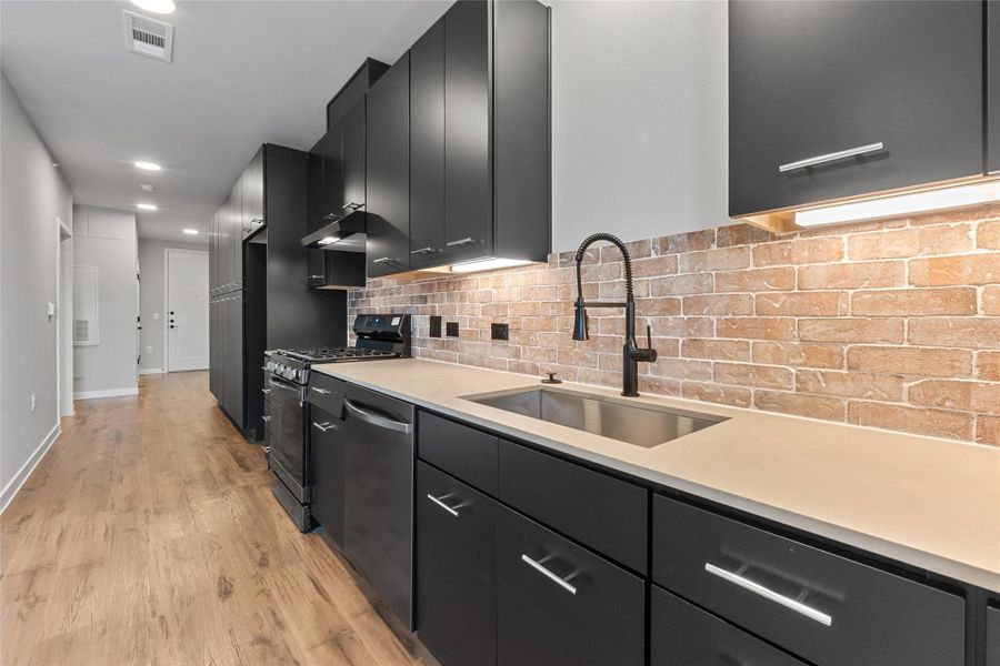 Kitchen with dark cabinetry, stainless steel appliances, light wood-type flooring, light countertops, and backsplash