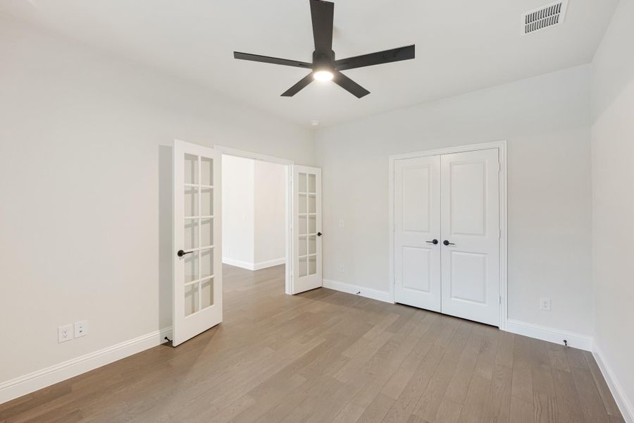 Empty bedroom with hardwood floors, black ceiling fan, French doors, and double closet doors Empty bedroom with hardwood floors, black ceiling fan, French doors, and double closet doors