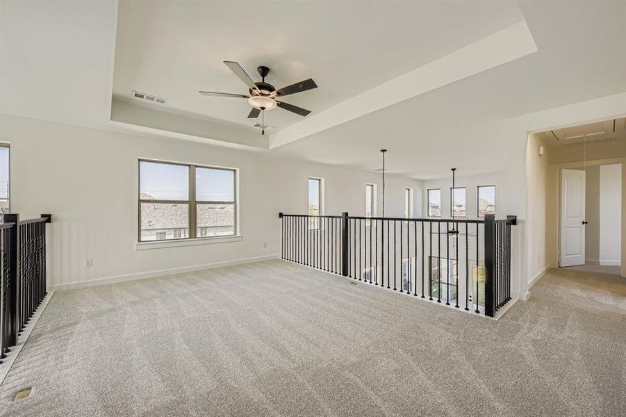 Carpeted spare room featuring attic access, a tray ceiling, and a ceiling fan