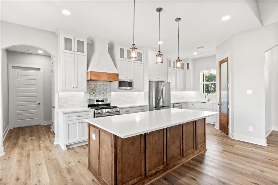 Kitchen with white cabinetry, glass insert cabinets, backsplash, a kitchen island, and recessed lighting Kitchen with white cabinetry, glass insert cabinets, backsplash, a kitchen island, and recessed lighting