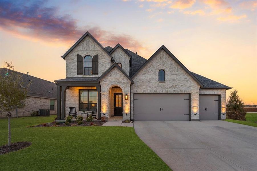 French provincial home featuring brick siding, a porch, central AC unit, driveway, and a front lawn