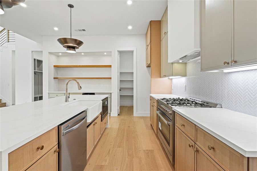 Kitchen with appliances with stainless steel finishes, light wood-style floors, tasteful backsplash, light stone counters, and a kitchen island with sink