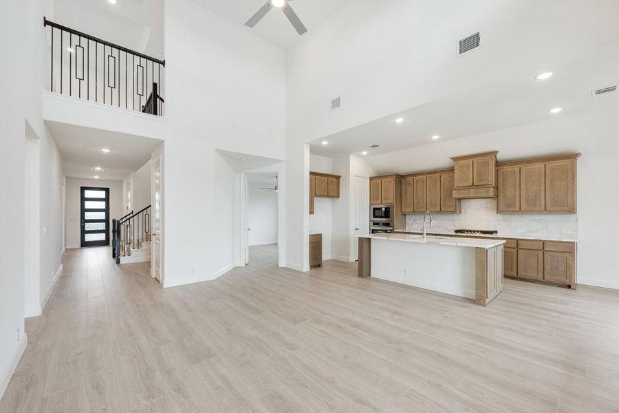 Open-concept living area with two-story ceiling, kitchen with wood cabinets and island, and light wood floors Open-concept living area with two-story ceiling, kitchen with wood cabinets and island, and light wood floors