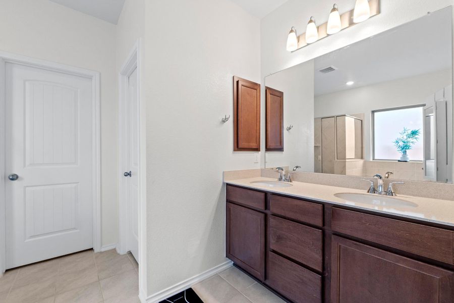 Bathroom featuring a dual vanity with dark wood cabinetry and a light-toned countertop, two integrated sinks with chrome faucets, and a large mirror with a four-light fixture