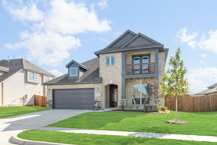 Two-story brick home with gray trim, second-floor balcony, two-car garage, and manicured front lawn